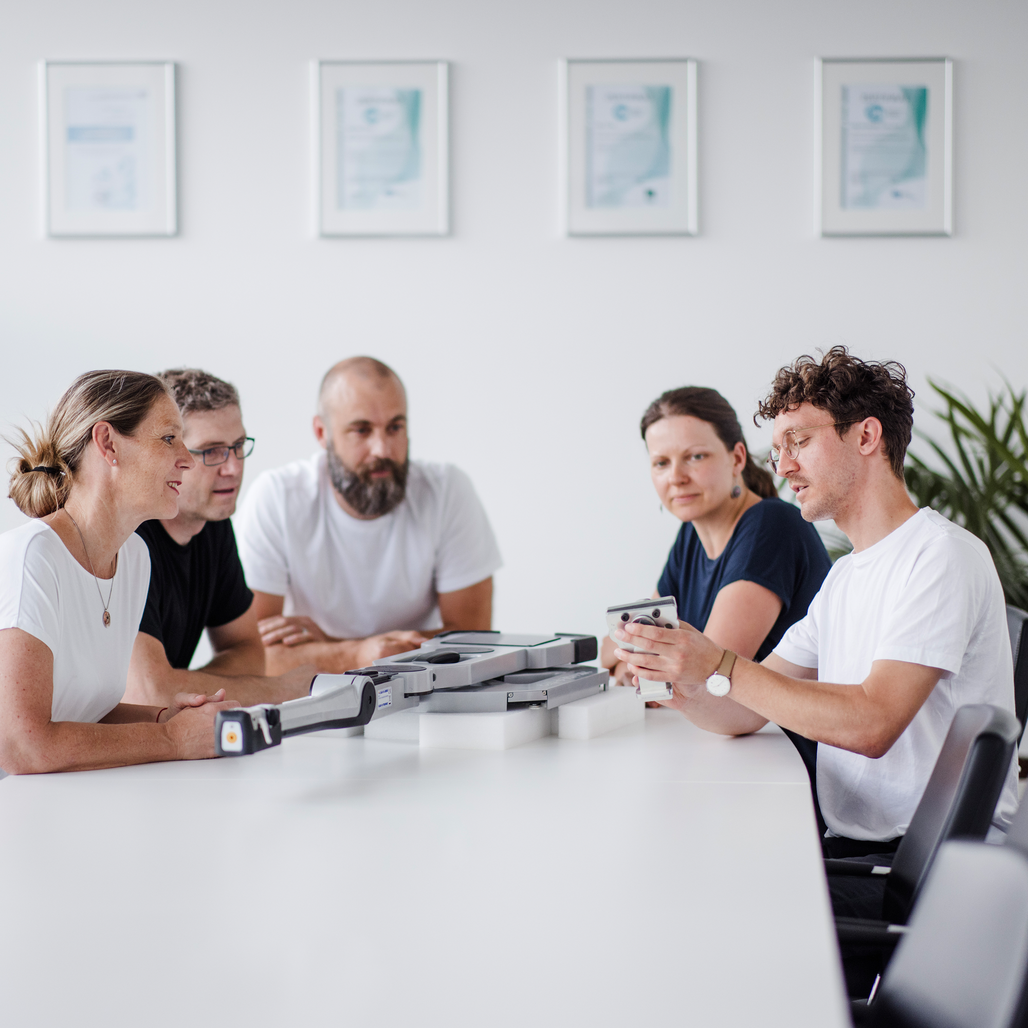 Teambesprechung über technische Komponenten Eine Gruppe von fünf Mitarbeitern sitzt an einem Konferenztisch und bespricht technische Komponenten, die auf dem Tisch vor ihnen liegen.