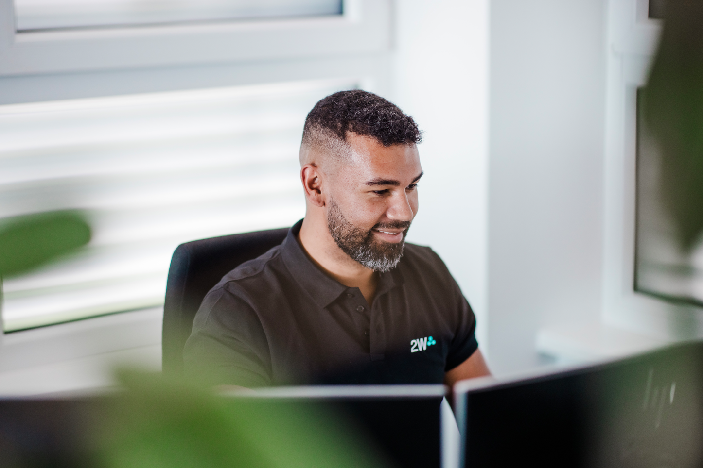 Erstellung einer individuellen Datenanalyse am Computer Ein 2W-Mitarbeiter sitzt lächelnd an einem Schreibtisch und arbeitet konzentriert an einem Computer um eine Kundenspezifische Datenanalyse zu erstellen.