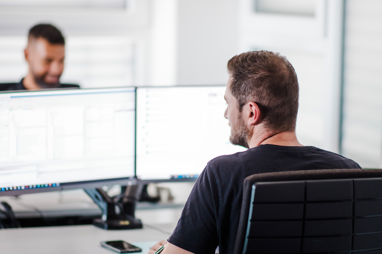 Automatisierte Datenanalyse im Büro Zwei Mitarbeiter arbeiten an Computern in einem modernen Büro. Sie nutzen individuelle Analysetools, um komplexe Daten effizient zu verarbeiten.