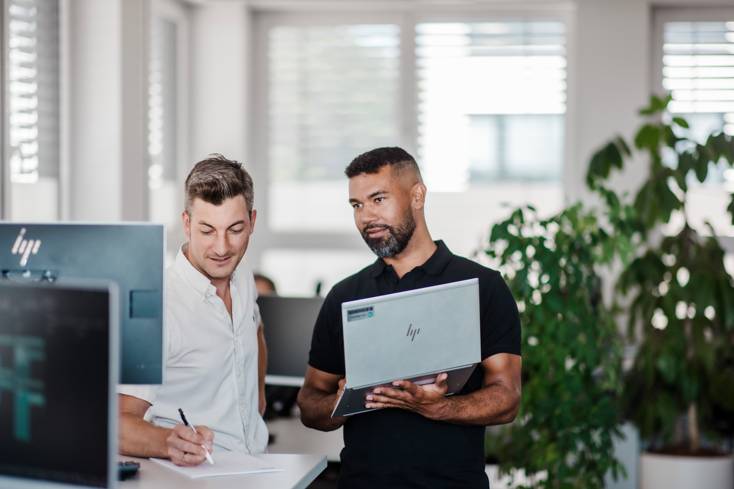 Überprüfung technischer Dokumentation von zwei Mitarbeitern Zwei Kollegen vergleichen technische Dokumentationen auf einem Computer und einem Laptop, um ihre Richtigkeit zu überprüfen.