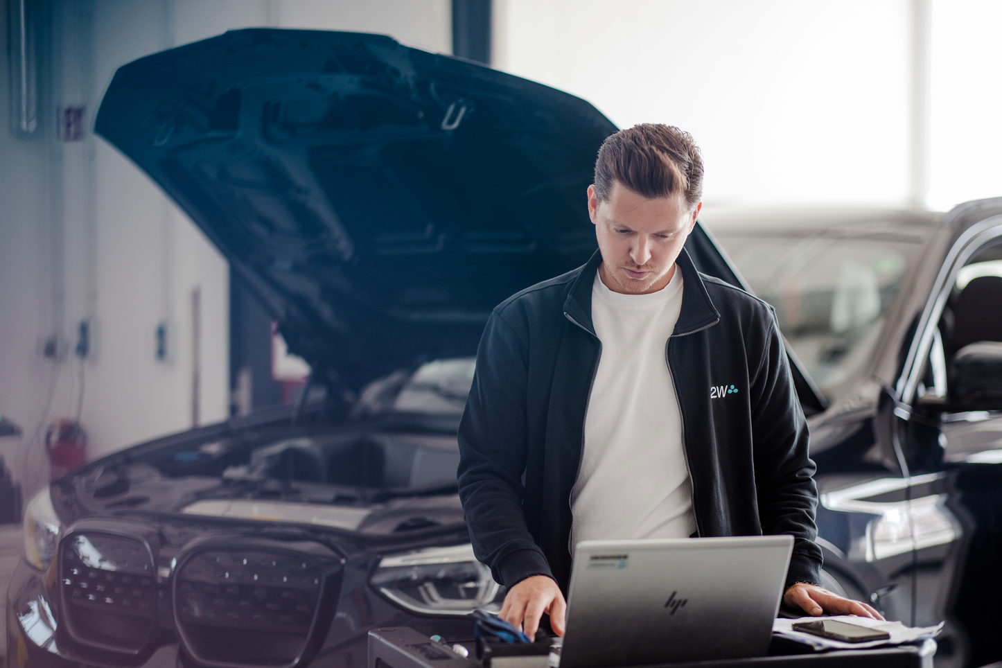 2W Mitarbeiter bei der Fahrzeugdiagnose mit einem Laptop 2W Mitarbeiter führt Fahrzeugdiagnose durch in einer moderne Werkstattumgebung