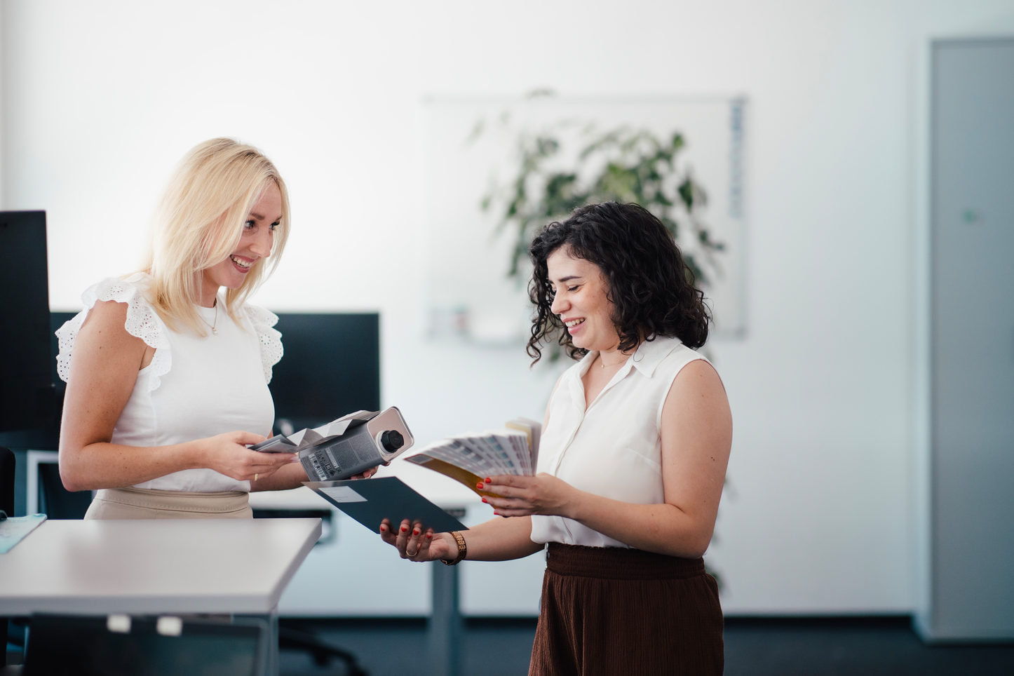 Kolleginnen stimmen sich zu Farbpaletten ab Zwei Frauen vergleichen Farben mit Hilfe von Farbfächern im Büro