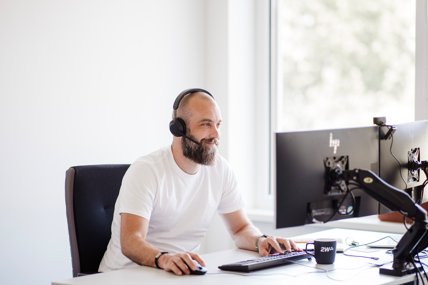 Erfolgreiche Kundenkommunikation Ein 2W-Mitarbeiter mit Headset sitzt vor einem Computerbildschirm und berät Kunden.