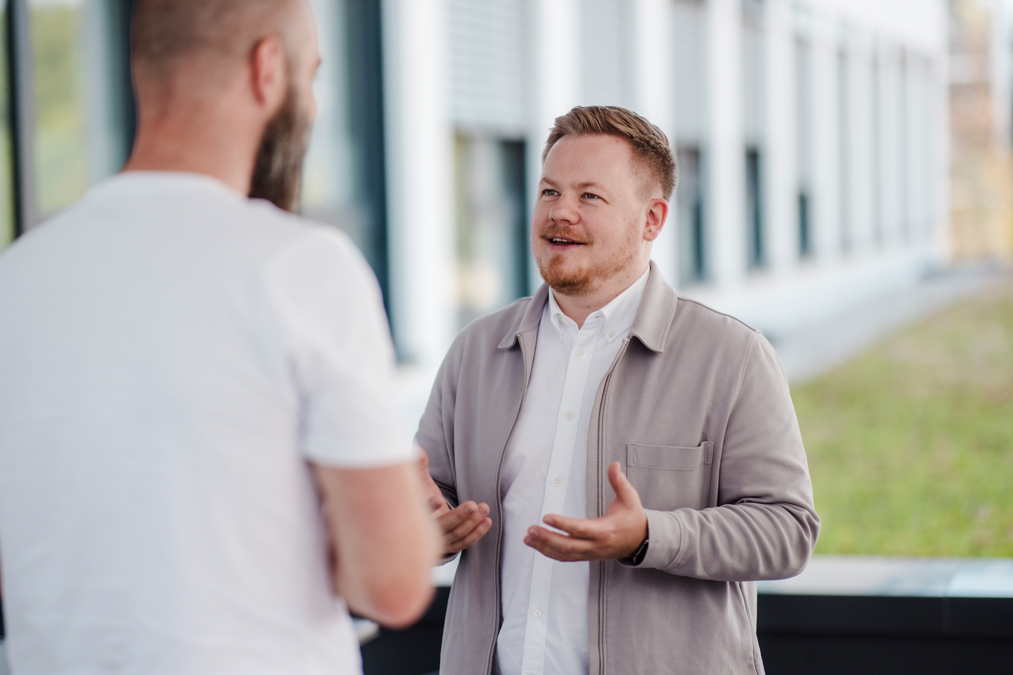Gespräch zwischen Kollegen im Freien Zwei Kollegen unterhalten sich entspannt vor einem modernen Bürogebäude.