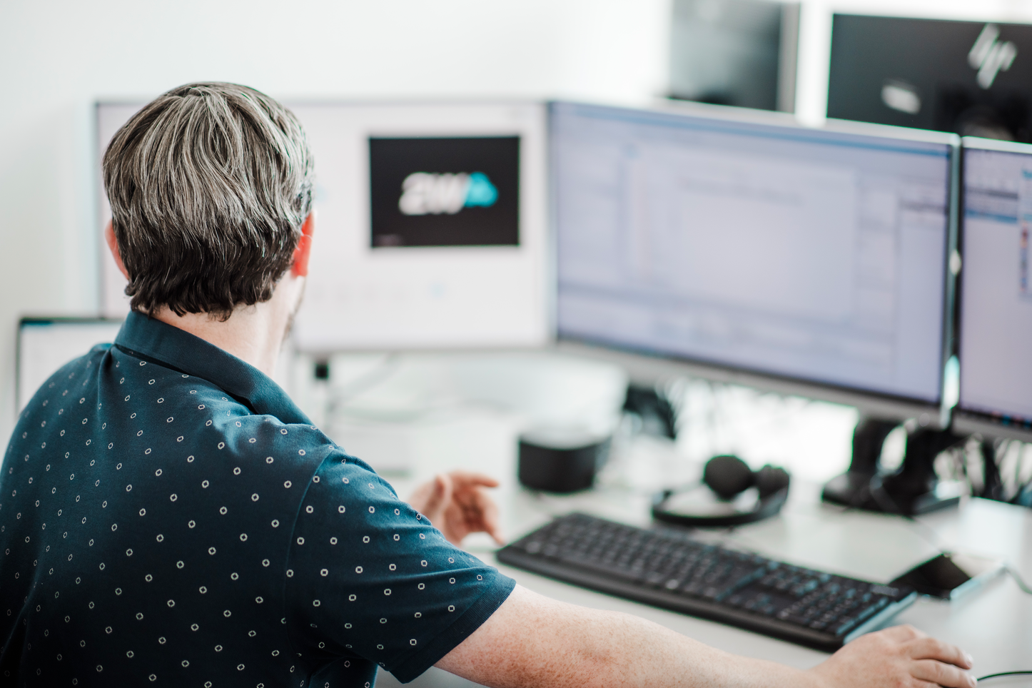 Mitarbeiter bei der Arbeit vor einem Computer mit 2W-Logo Mitarbeiter von hinten bei der Arbeit vor einem Computer mit unscharfem Bildschirm und 2W-Logo.